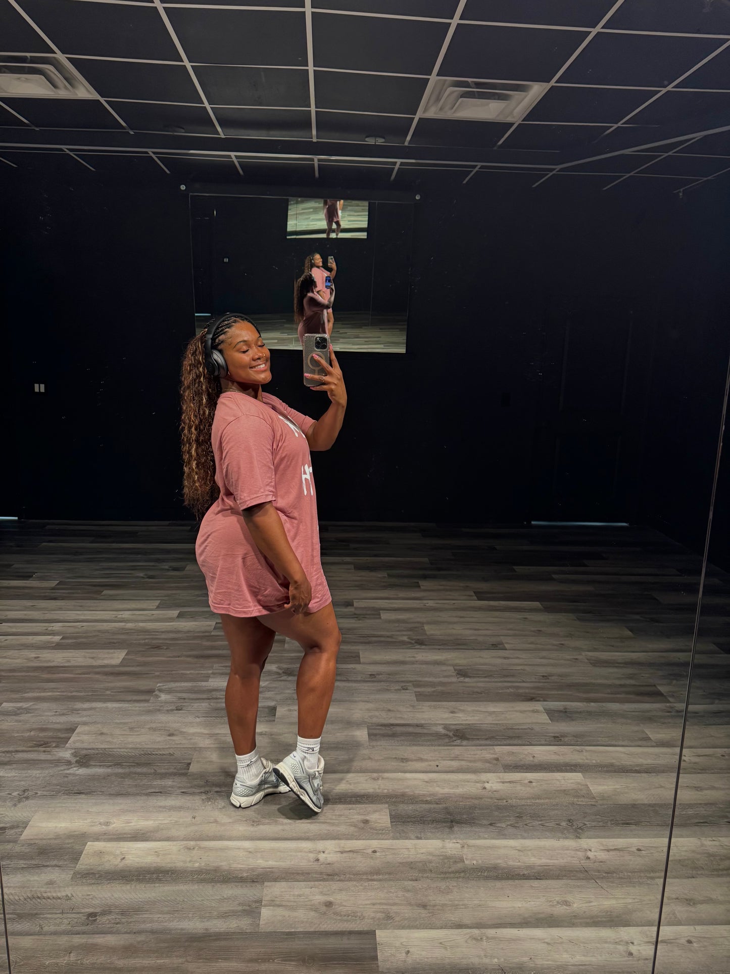 Person taking a mirror selfie in a room with dark walls and wooden floor.